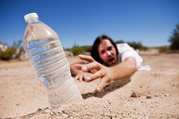 dehydrated man crawling through the desert reaching for bottle of water.