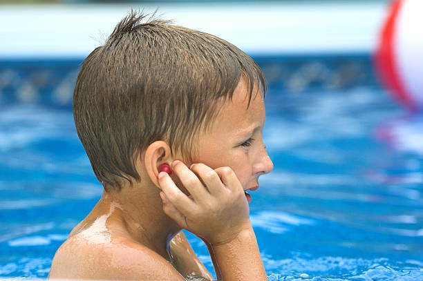 young boy making sure his earplugs are in while playing in the pool